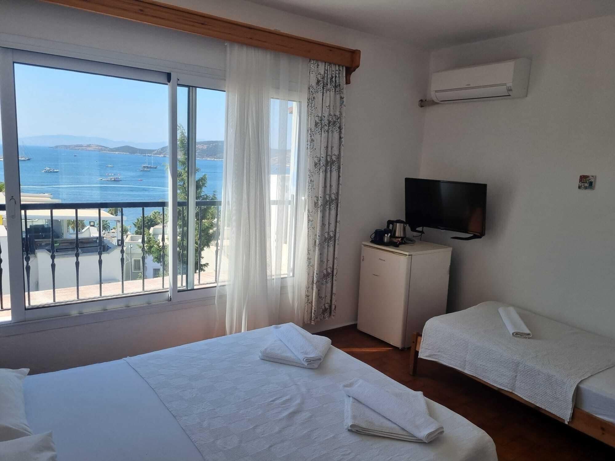 Habitación de hotel con balcón, televisión, refrigerador pequeño y dos camas.
