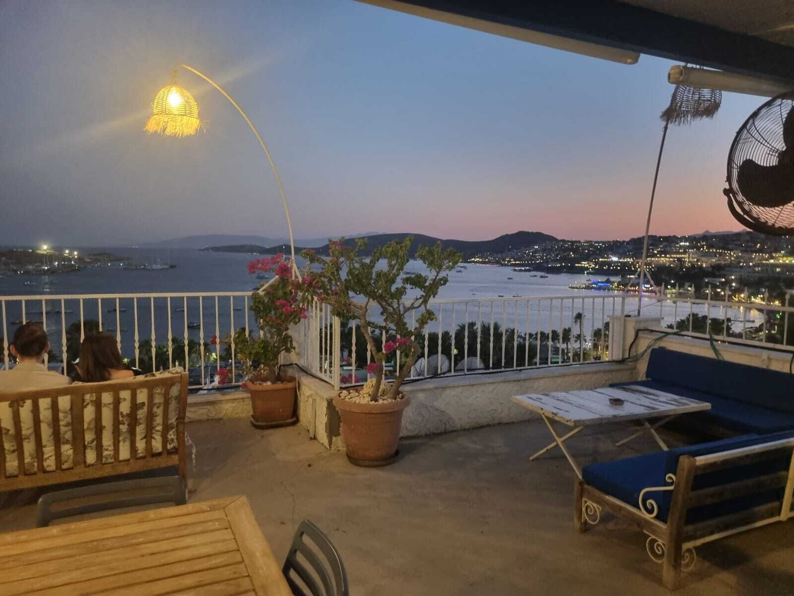Un balcón con vista al mar, una mesa, sillas y plantas en macetas.