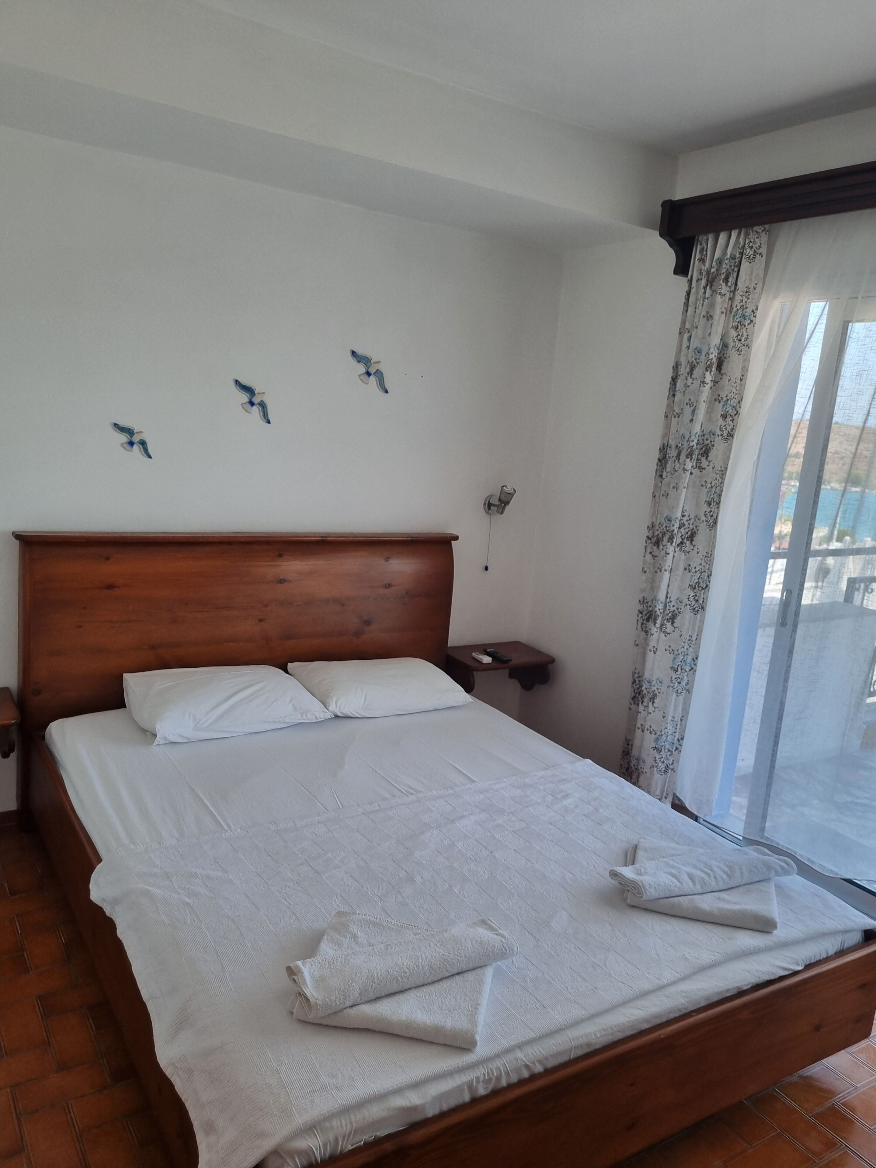 Een net opgemaakt bed met witte lakens en handdoeken, een houten hoofdbord en een nachtkastje met een afstandsbediening.