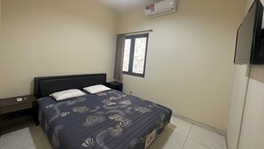 Un dormitorio con cama, mesita de noche, ventana y aire acondicionado.