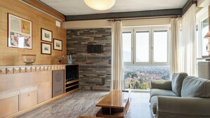 Un salon doté d’une cheminée en pierre, d’un canapé, d’une table basse et offrant une vue sur le paysage urbain grâce à de grandes fenêtres.
