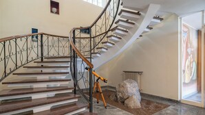 Un escalier en colimaçon avec une rampe en métal et des marches en bois, menant à un palier où se trouvent un gros rocher et un radiateur.