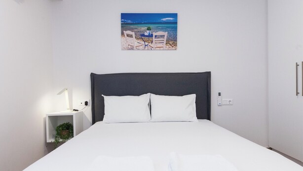 A neatly made bed with white linens and two folded towels, a bedside lamp, and a small plant on a nightstand. - Kipseli New Modern Cosy Apts Apt No 5 (Athens)
