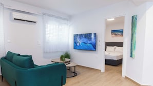 A modern living room with a teal sofa, a flat-screen TV, a small round table, and a bed in the adjacent room. - Kipseli New Modern Cosy Apts Apt No 5 (Athens)