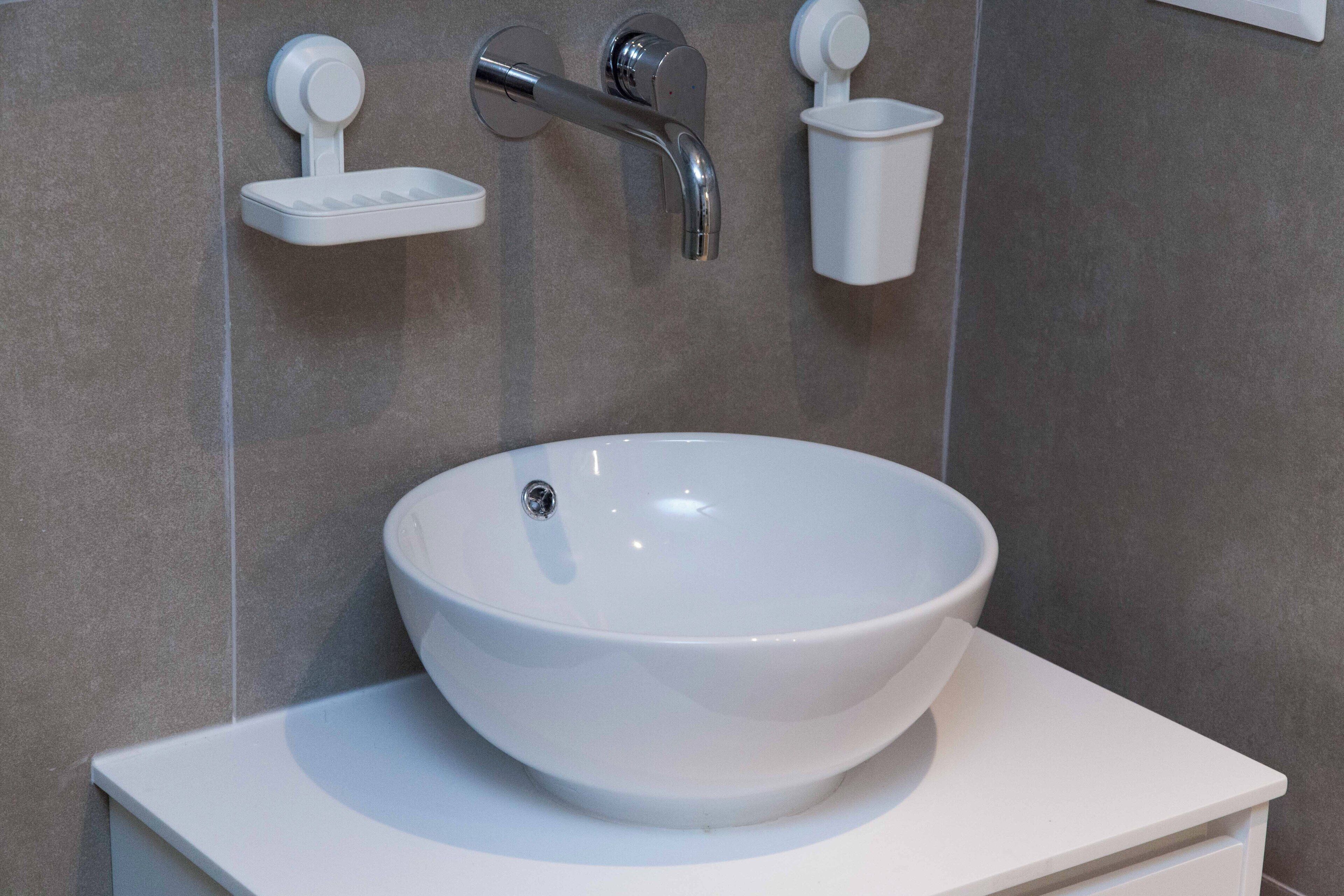 Un bagno con un lavandino bianco, un rubinetto cromato e due piccoli dispenser di sapone bianchi a parete.