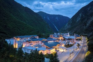 Un hotel con varias edificaciones, una plaza central y un camino que se adentra en las montañas.