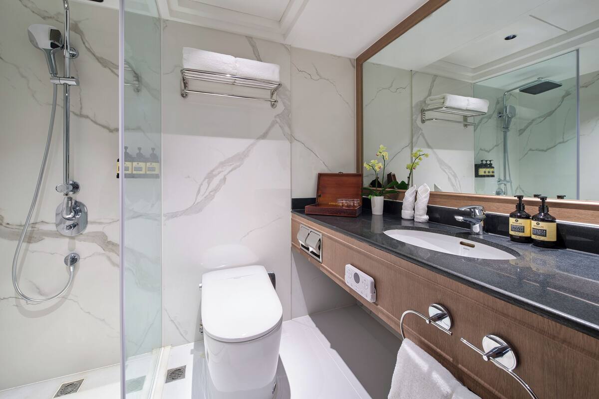 Ein modernes Badezimmer mit einer gläsernen Dusche, einer weißen Toilette, einem Waschtisch mit Marmorplatte und einem großen Spiegel.