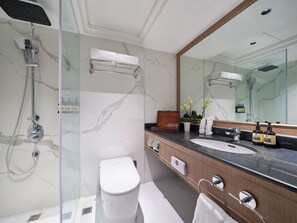 Une salle de bain moderne avec une douche à parois de verre, des toilettes blanches, un meuble-lavabo avec un plan de travail en marbre et un grand miroir.