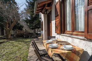 Un espace de restauration en plein air avec une table dressée pour quatre personnes, des bancs et une statue en arrière-plan.