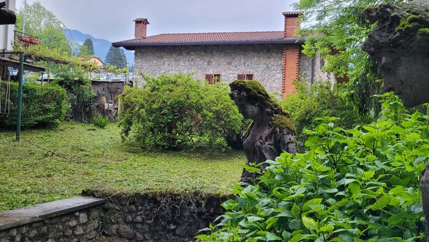 A stone house with a red roof, surrounded by lush greenery and a large rock formation.