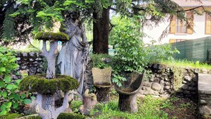 A garden with a statue, stone structures, and a building in the background.