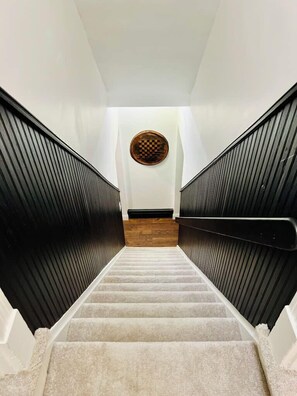Eine Treppe mit schwarzen Geländern und Teppichboden, die zu einer Zwischenebene mit Holzboden und einer runden Wanddekoration führt.
