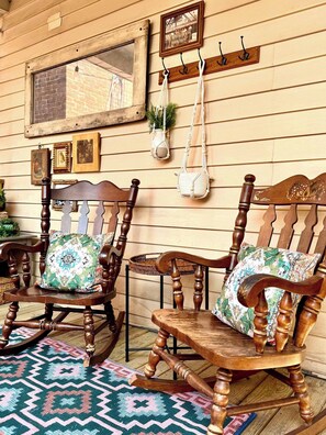 A wooden rocking chair with a patterned cushion, a wooden table, and a patterned rug on a wooden floor.