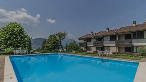 A swimming pool with lounge chairs, a view of mountains, and a building with balconies. - SunsetView - Lake Como swimming pool and garden (Lierna)