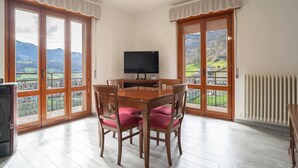 Un coin repas avec une table et des chaises, un téléviseur et de grandes fenêtres donnant sur la campagne.