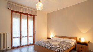 Une chambre à coucher avec un lit en bois, deux tables de chevet avec des lampes, un radiateur et une grande fenêtre avec des rideaux.