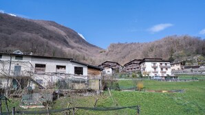 Un village rural aux maisons traditionnelles, sous un ciel dégagé, avec des montagnes en toile de fond.