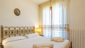 Hotelkamer met een bed, nachtkastje, lamp, raam met gordijnen en een radiator.