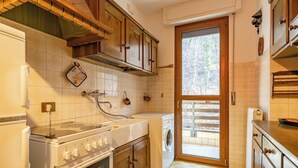Een kleine keuken met een kookplaat, oven, wasmachine en houten keukenkastjes.