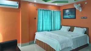 A bedroom with orange walls, a bed with white bedding, a ceiling fan, and a window with curtains. - Raj Hotel (Baksa)