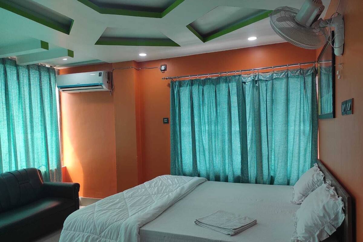 A hotel room with a bed, a sofa, teal curtains, and a ceiling fan.