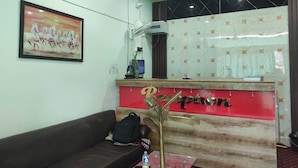 A reception area with a reception desk, a framed painting, a brown sofa, and a decorative plant. - Raj Hotel (Baksa)