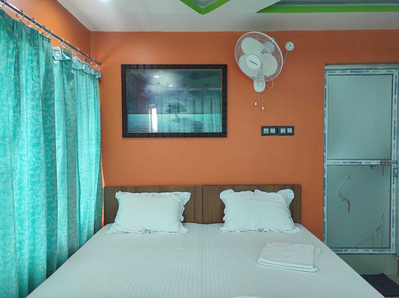 A bedroom with a bed, a wall-mounted fan, a framed picture, and a wardrobe.