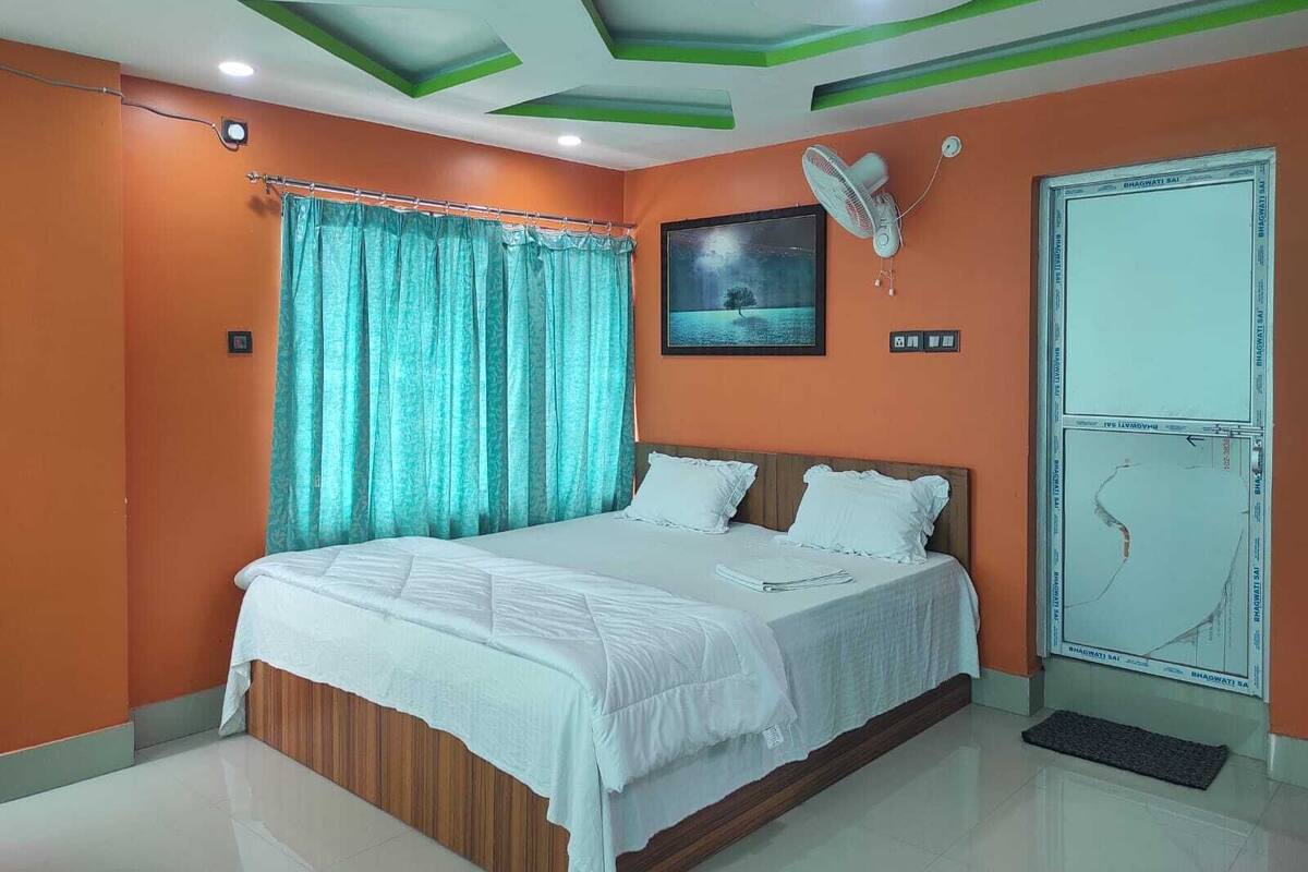 A bedroom with a bed, curtains, a fan, and a wall-mounted picture.