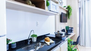 Une cuisine moderne avec un plan de travail noir, un évier en acier inoxydable et une miche de pain posée sur une planche à découper. Des plantes en pot sont disposées sur les étagères et un téléviseur à écran plat est fixé au mur.