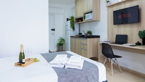 Une chambre d’hôtel moderne équipée d’un lit, d’un bureau avec un ordinateur portable, d’une télévision et d’un mini-bar.