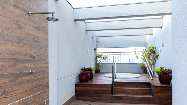 Un escalier moderne avec des marches en bois et des rampes en métal, menant à un balcon agrémenté de plantes en pot et offrant une vue sur la ville.