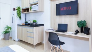 Une cuisine moderne équipée d’un four à micro-ondes, d’un réfrigérateur et d’un meuble en bois. On peut voir un ordinateur portable sur un bureau, ainsi qu’une plante et un téléviseur qui affiche « NETFLIX ».