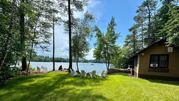 A cabin with a view of a lake, surrounded by trees and a grassy area with outdoor seating. - Winnipesaukee luxury waterfront 3-BDR home w/dock, views, AC, laundry, beach (Moultonborough)