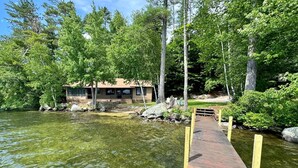A lakeside cabin with a dock leading to a small boat. - Winnipesaukee luxury waterfront 3-BDR home w/dock, views, AC, laundry, beach (Moultonborough)