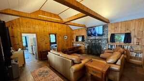A log cabin interior with a fireplace, leather sofas, a stone wall, and a television mounted above it. - Winnipesaukee luxury waterfront 3-BDR home w/dock, views, AC, laundry, beach (Moultonborough)