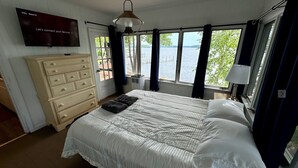 A bedroom with a bed, a dresser, a TV, and a window with a view of the water. - Winnipesaukee luxury waterfront 3-BDR home w/dock, views, AC, laundry, beach (Moultonborough)