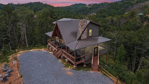 A modern cabin with a stone chimney, wooden deck, and a gravel driveway. - 2 Bedroom w/ Fire Pit, Indoor/Outdoor Fireplace, Hot Tub, Cornhole, Shuffleboard (Sevierville)