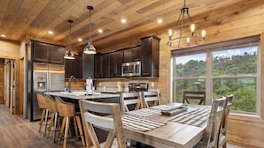 A modern kitchen with wooden cabinets, stainless steel appliances, and a large island with bar stools. - 2 Bedroom w/ Fire Pit, Indoor/Outdoor Fireplace, Hot Tub, Cornhole, Shuffleboard (Sevierville)