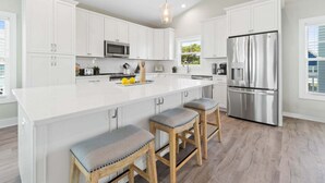 A modern kitchen with white cabinetry, a stainless steel refrigerator, and a large island with stools.