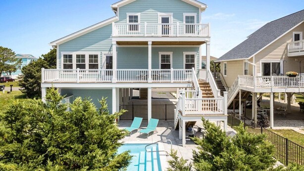 A two-story house with a balcony, a pool, and a covered patio area.