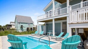 A swimming pool with lounge chairs and a covered area with tables and chairs.