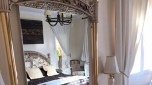 A bedroom with a large ornate mirror, a bed with a headboard, a bedside table with a lamp, and a dresser with drawers. - Boutique Villa Marbella (Marbella)