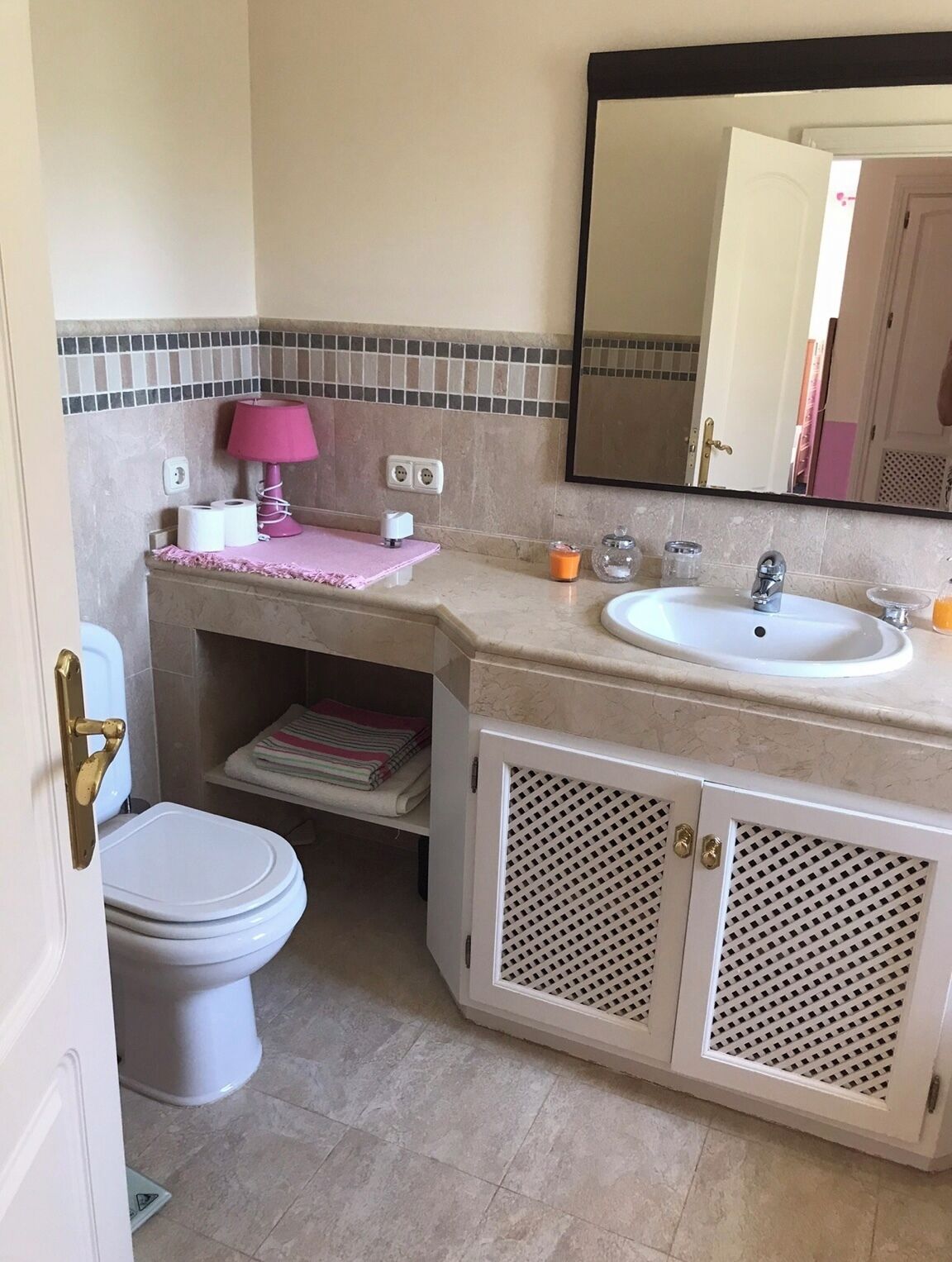 Ein Badezimmer mit Toilette, Waschbecken, Spiegel und einer pinkfarbenen Lampe auf dem Waschtisch.