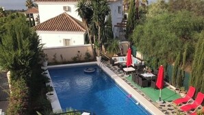 A swimming pool with a hot tub, surrounded by lounge chairs and umbrellas, with a view of a building and palm trees. - Boutique Villa Marbella (Marbella)