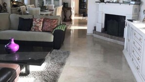 A living room with a sofa, coffee table, and fireplace. There is a television mounted above the fireplace and a chandelier hanging from the ceiling. - Boutique Villa Marbella (Marbella)