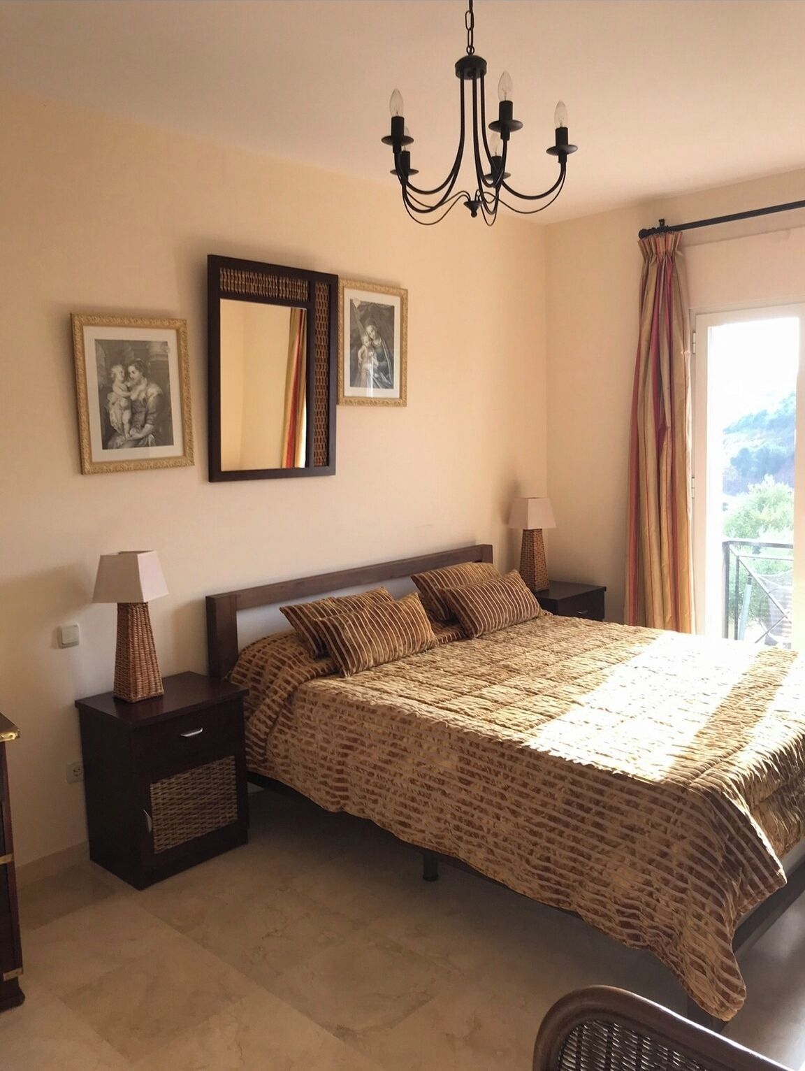 Une chambre à coucher avec un grand lit, deux tables de chevet, un lustre et des tableaux encadrés accrochés au mur.