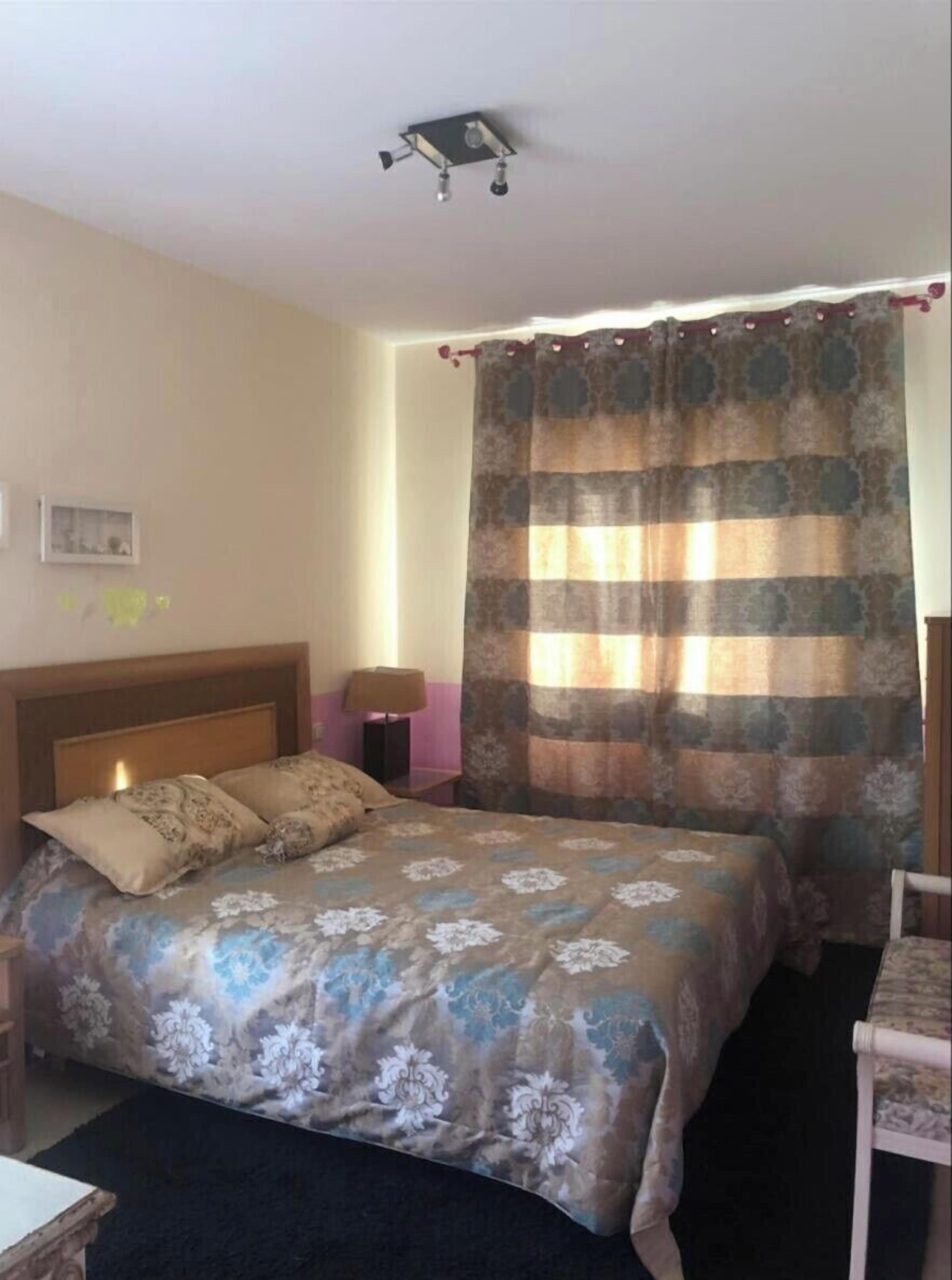 A bedroom with a bed, a nightstand, a lamp, and a window with curtains.