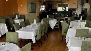 Ein Restaurant mit mehreren runden Tischen, die mit weißen Tischdecken bedeckt sind, grünen Polstersesseln und Holzböden.