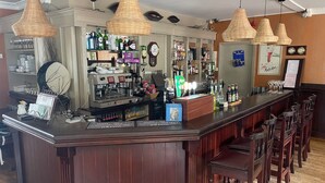 Eine Bar mit einer Theke, Barhocker, hängenden Lampen und verschiedenen Flaschen und Gläsern.