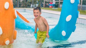 Een kind speelt in een waterpark met hoge, kleurrijke glijbanen.